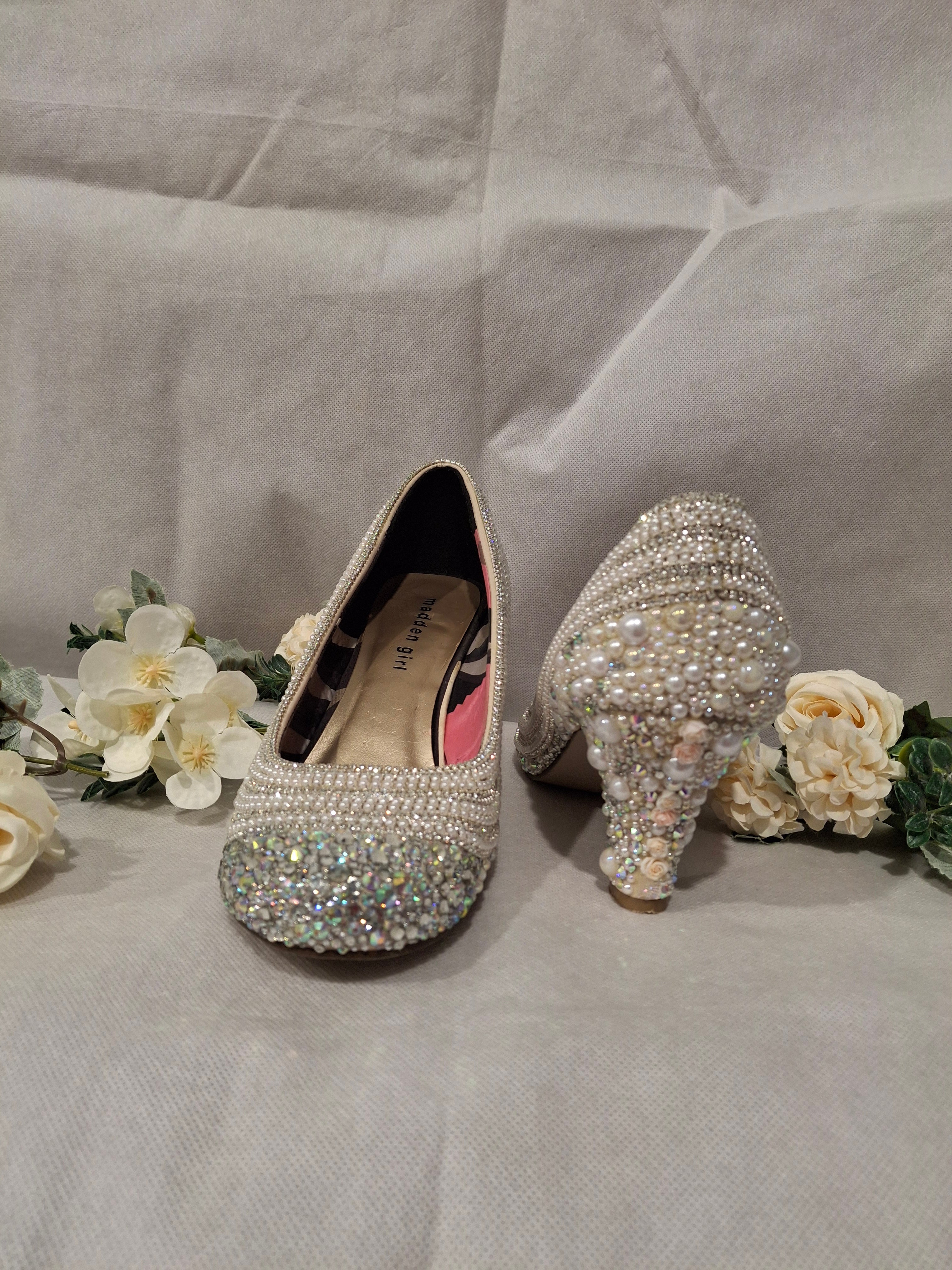 Pair of embellished high-heeled shoes on a light fabric background with flowers.