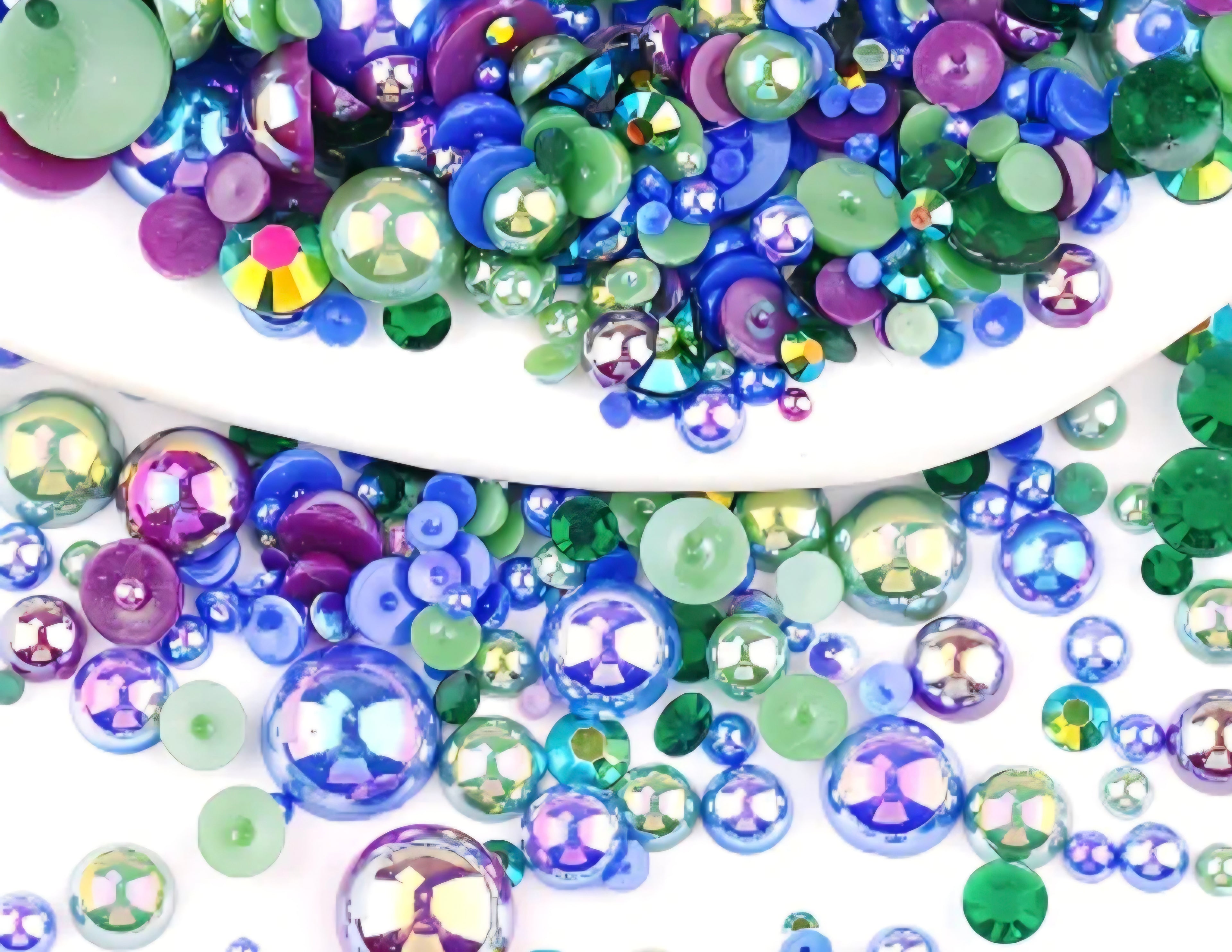 Assorted colorful round pearls and rhinestones in green, blue, and purple on a white background