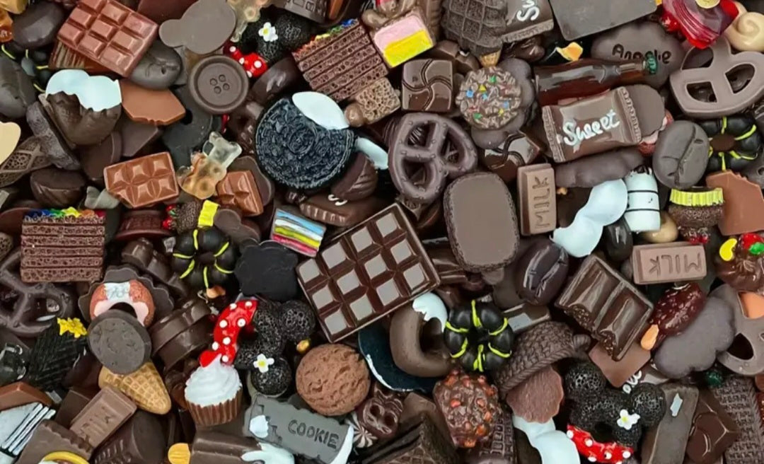 Assorted chocolate charms including cookies, pretzels, and other shapes on a dark background