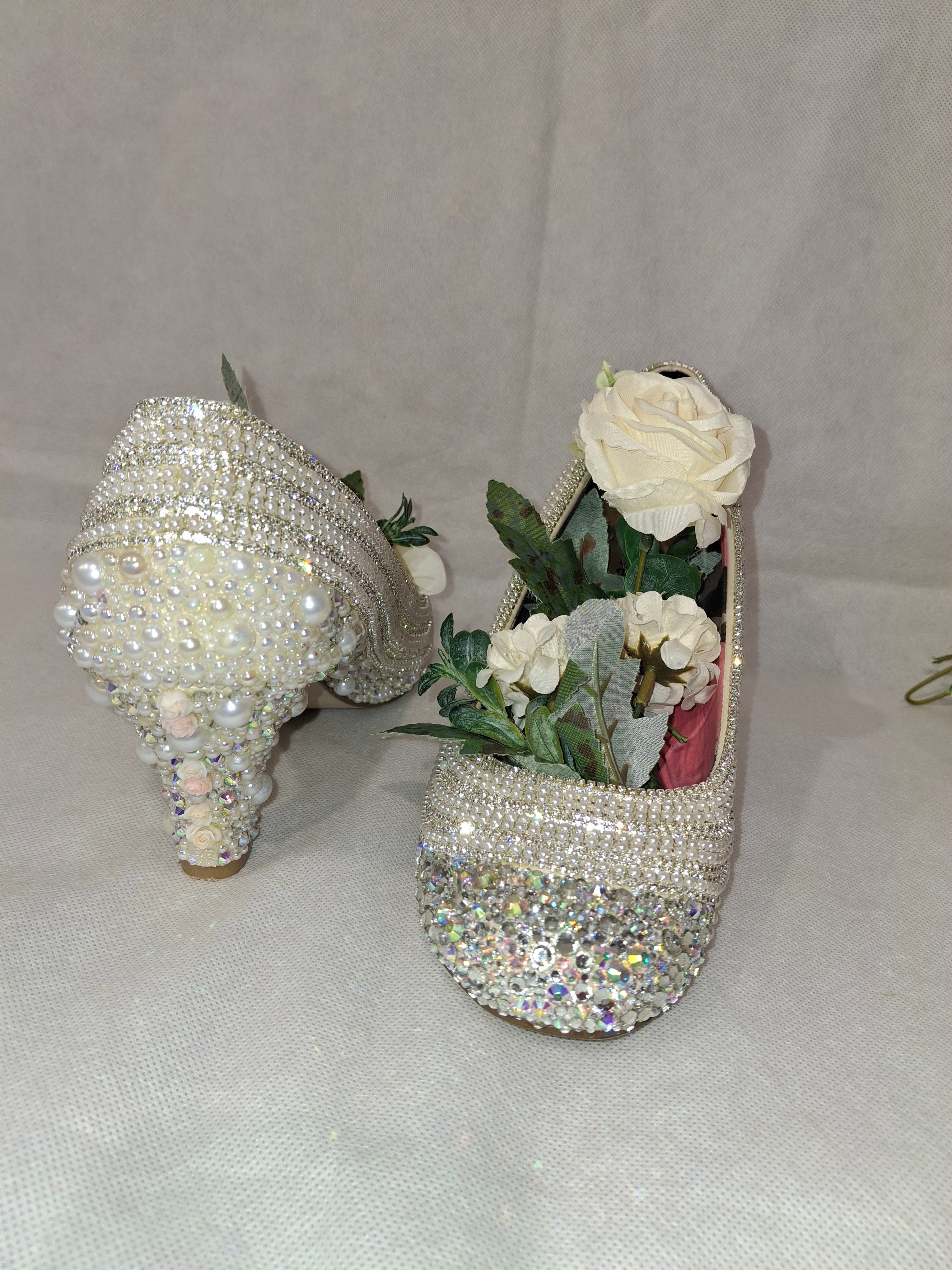Sparkly high-heeled shoes with floral decorations on a light gray background