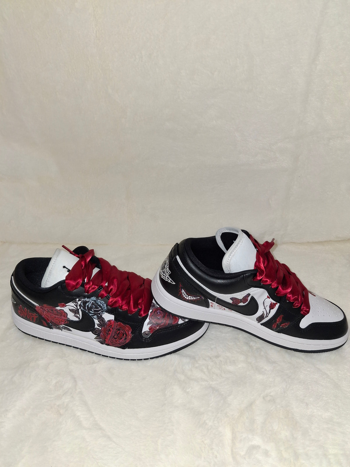 A pair of custom low-top sneakers with a black and white base, featuring red satin laces, red roses