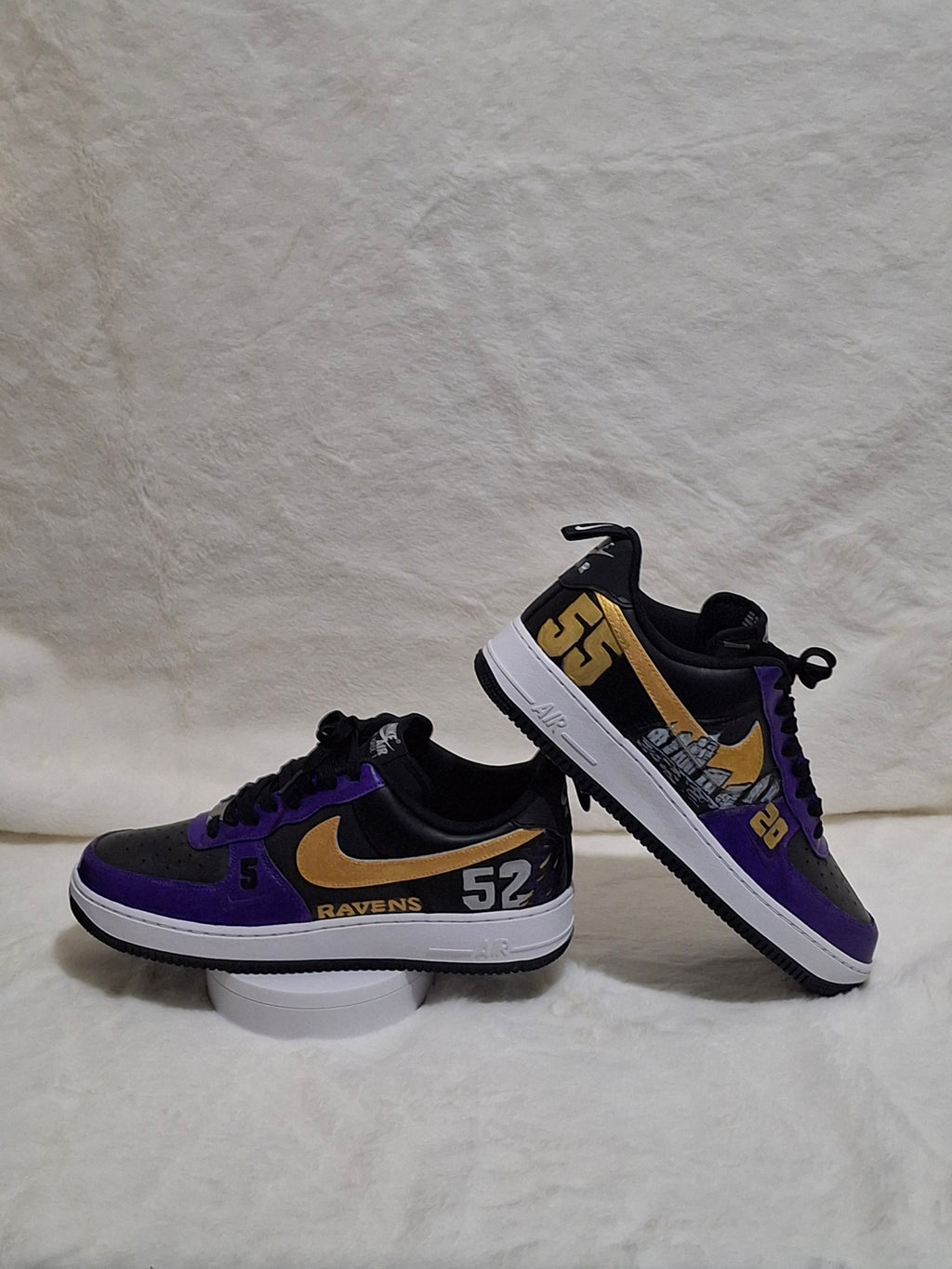 A pair of custom Nike Air Force 1 style sneakers in black, purple, and gold details on both sides. 