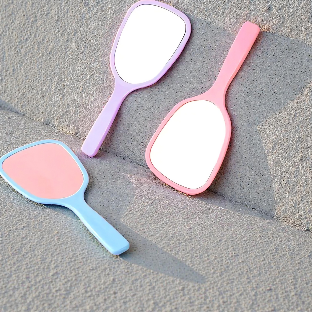 Three handheld mirrors in pink, blue, and purple on a textured surface.