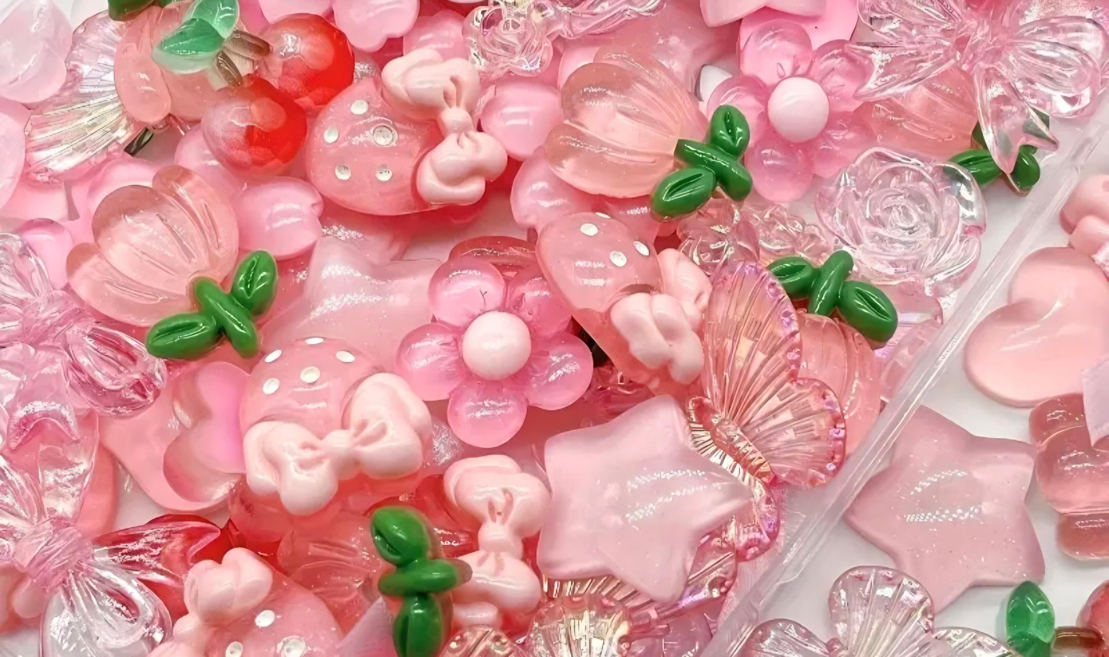 Assorted pink and green decorative charms including flowers and bows in a box.