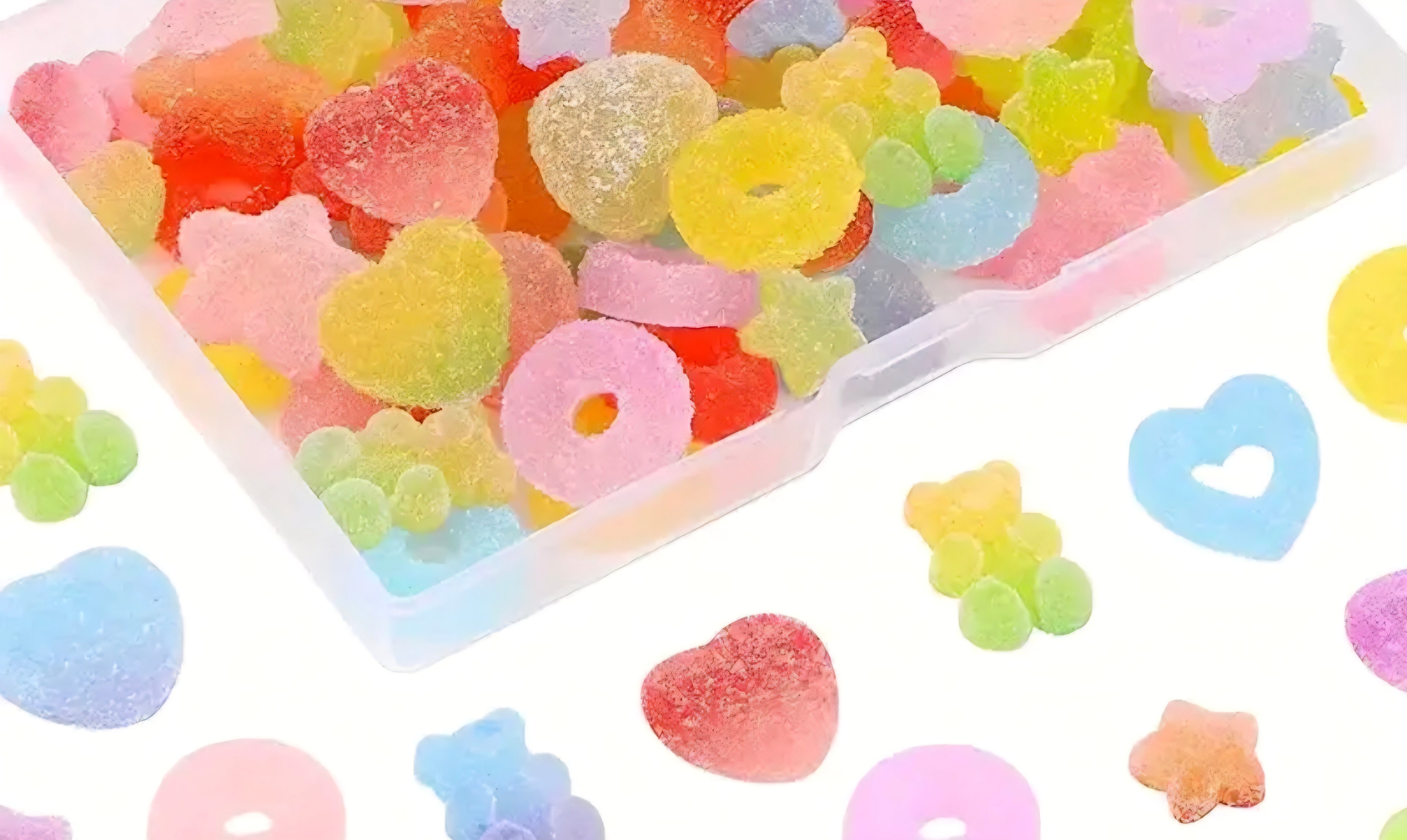 Colorful gummy candies charms in a transparent container with various shapes on a white background.