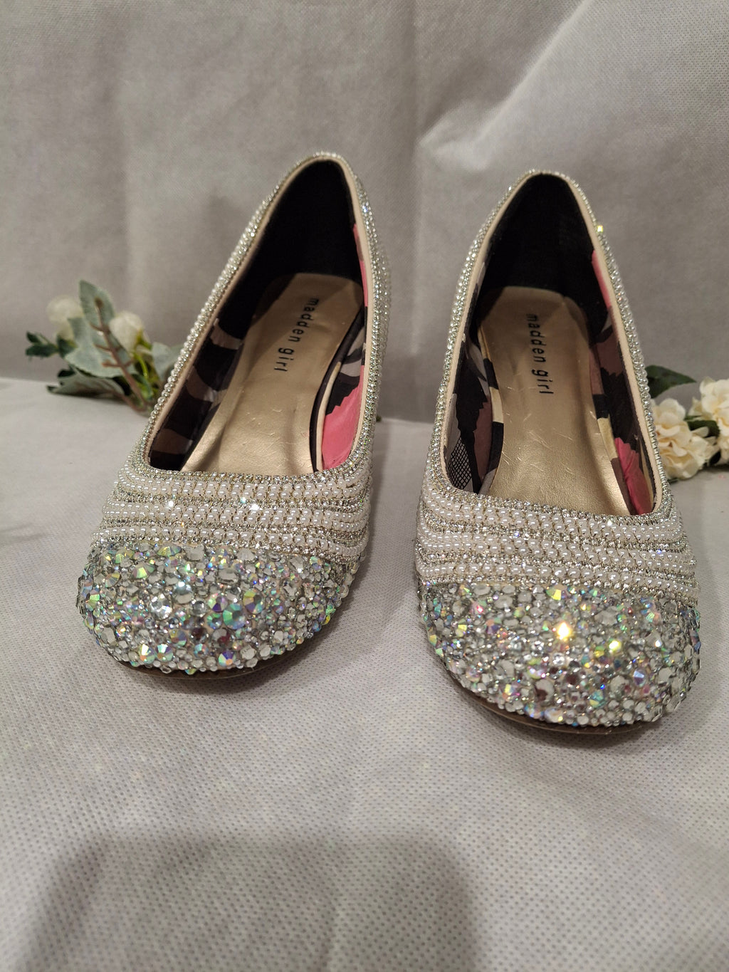 Pair of high-heeled shoes with sparkling embellishments on a light gray background