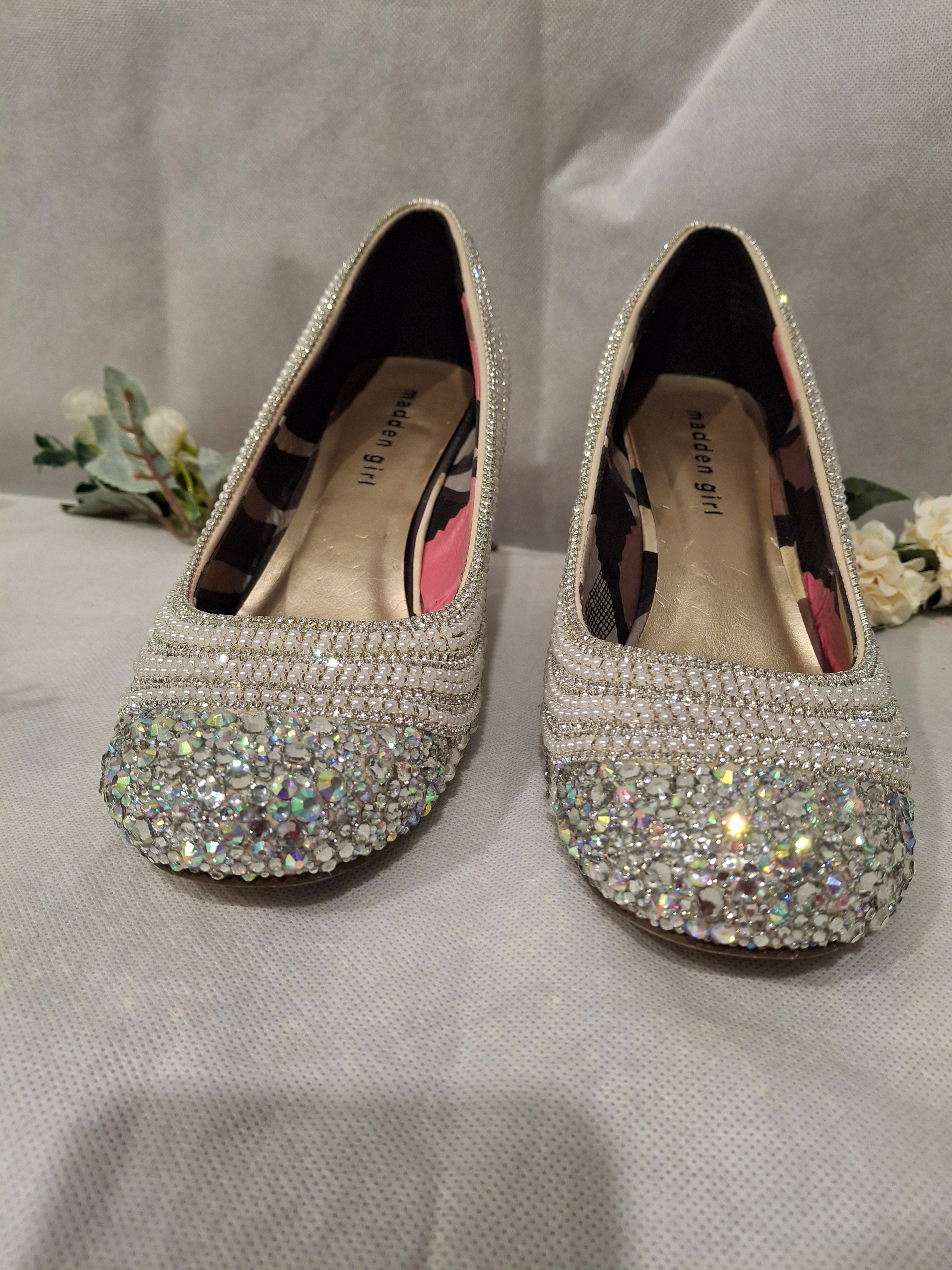 Pair of high-heeled shoes with sparkling embellishments on a light gray background