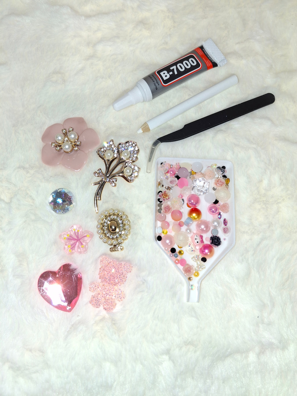 DIY junk case kit with pink coquette charms, rhinestones, B-7000 glue, and tweezers on white surface