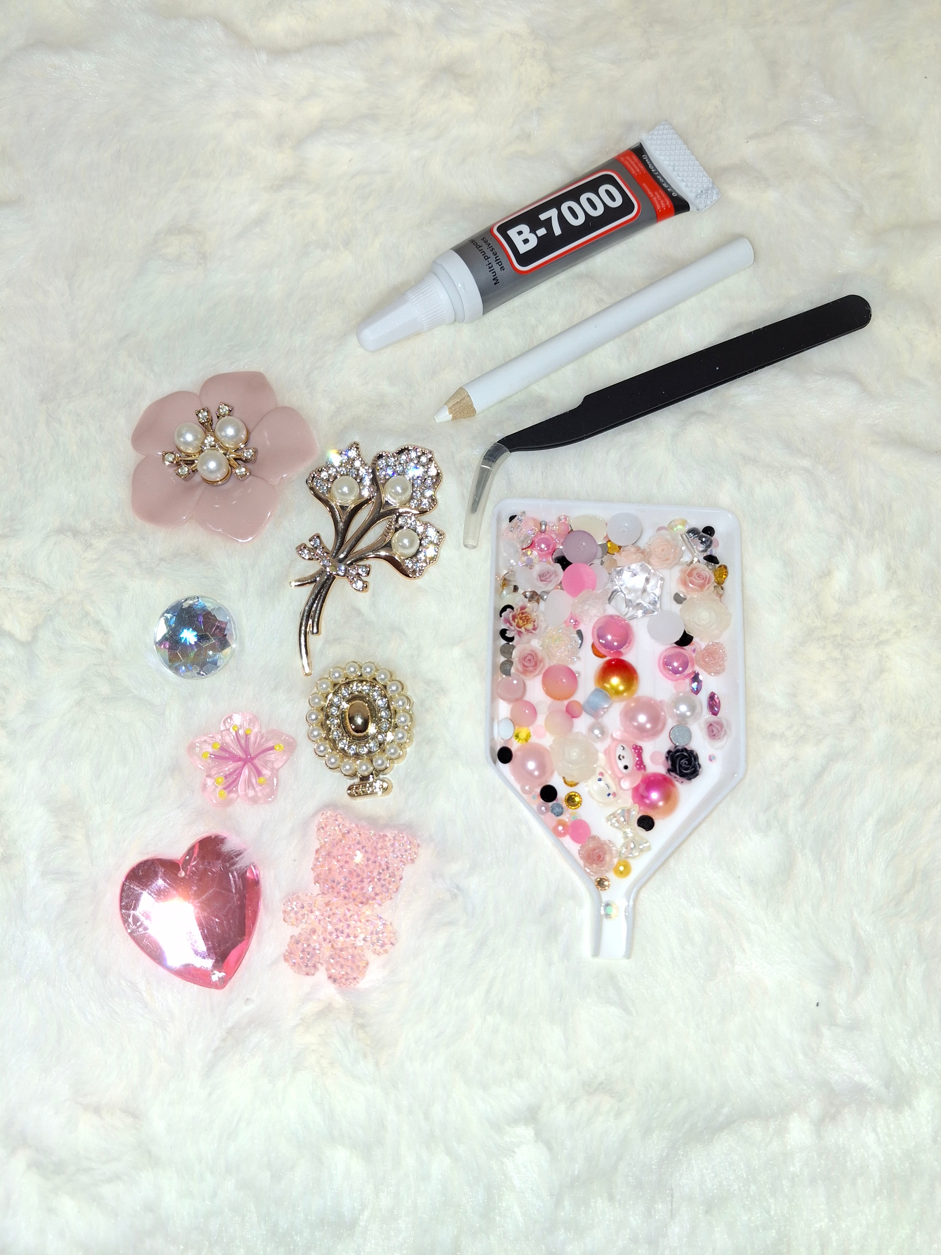 DIY junk case kit with pink coquette charms, rhinestones, B-7000 glue, and tweezers on white surface